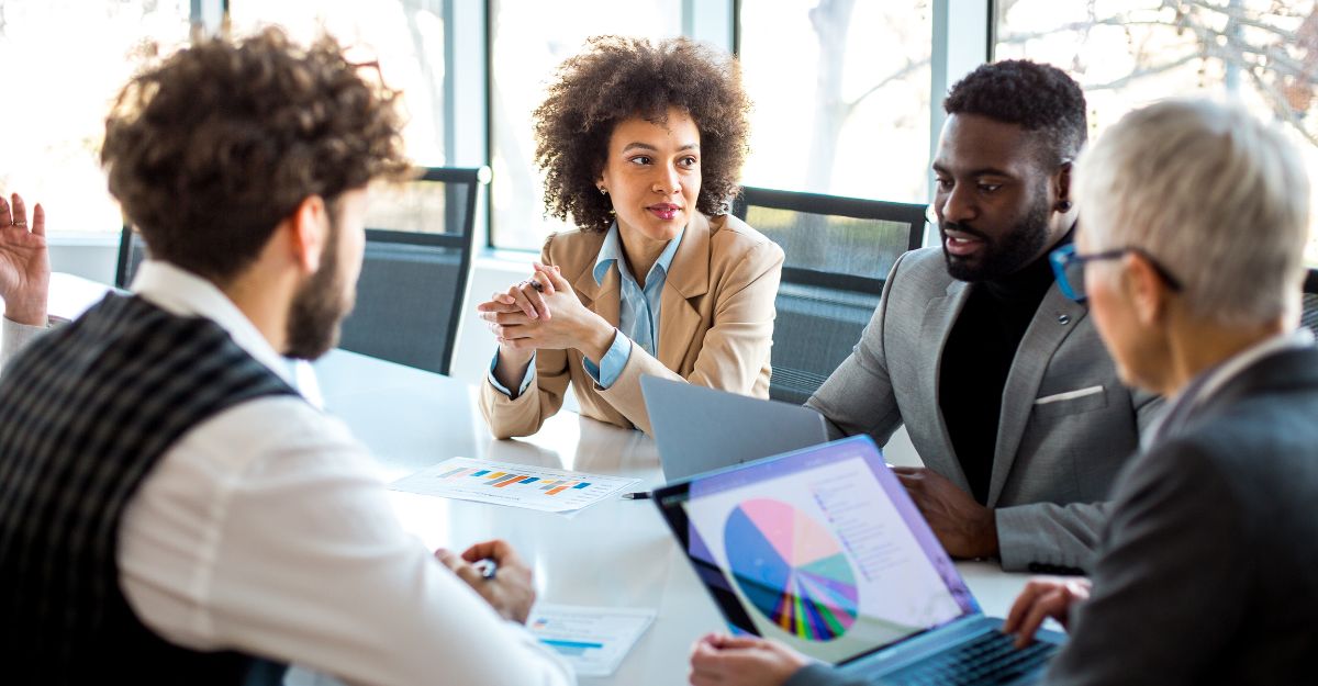 Four colleagues reviewing printed charts and laptops around a boardroom table